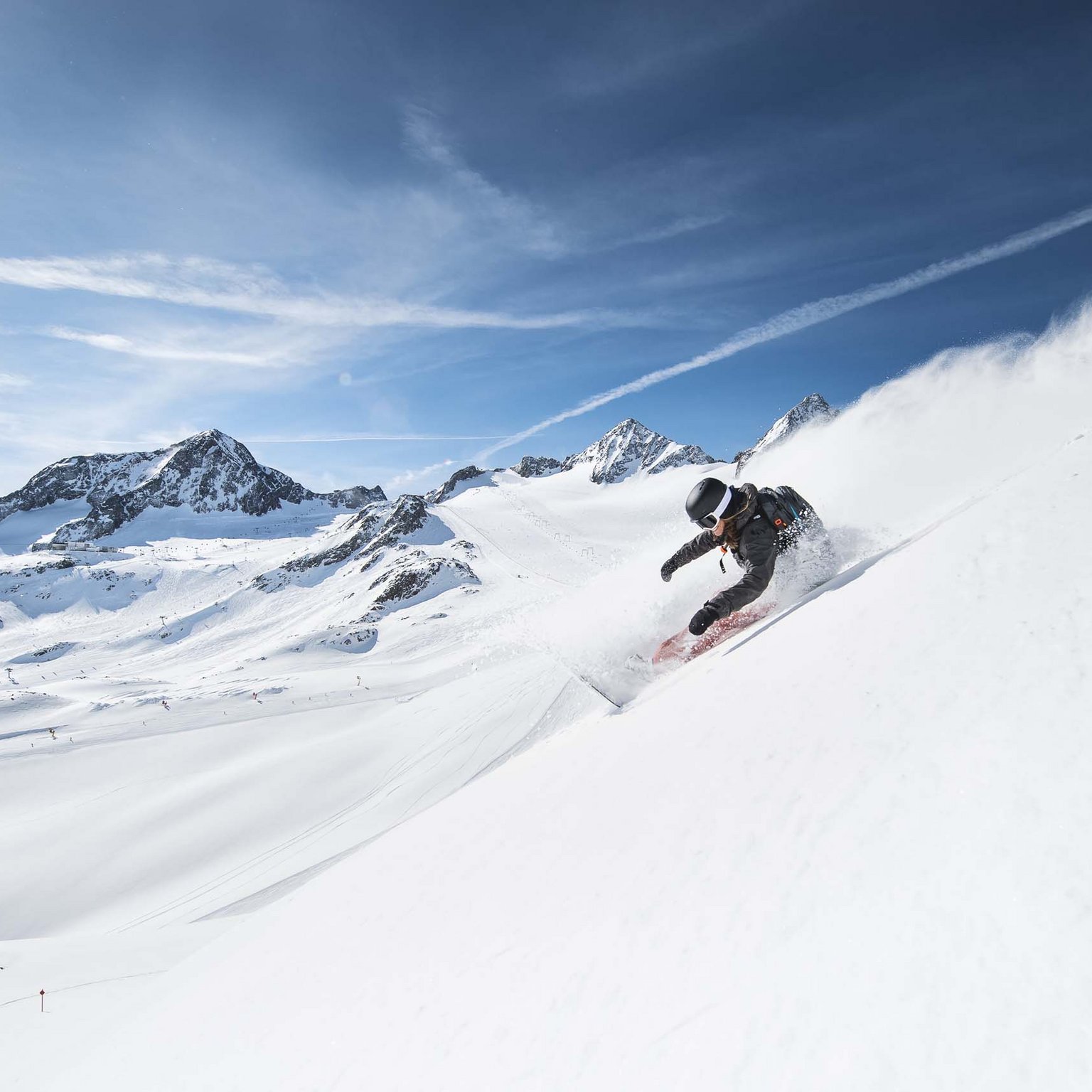Stubaital: das Hotel mit Pool Snowboarder fährt steil den verschneiten Berg im Sonnenschein hinab
