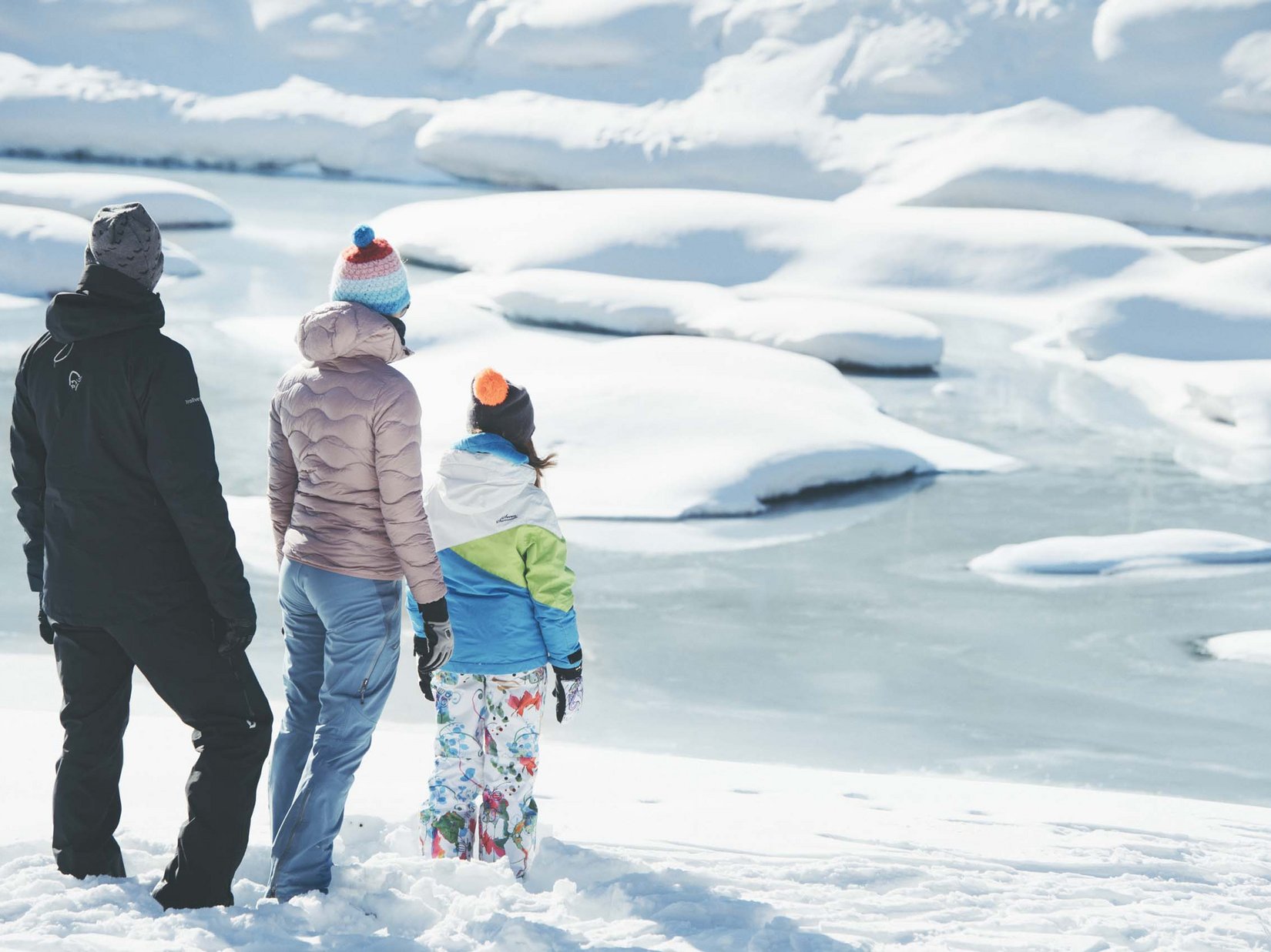 Stubaital: das Hotel mit Pool Drei Personen in Winterkleidung stehen im Schnee und blicken auf einen zugefrorenen See