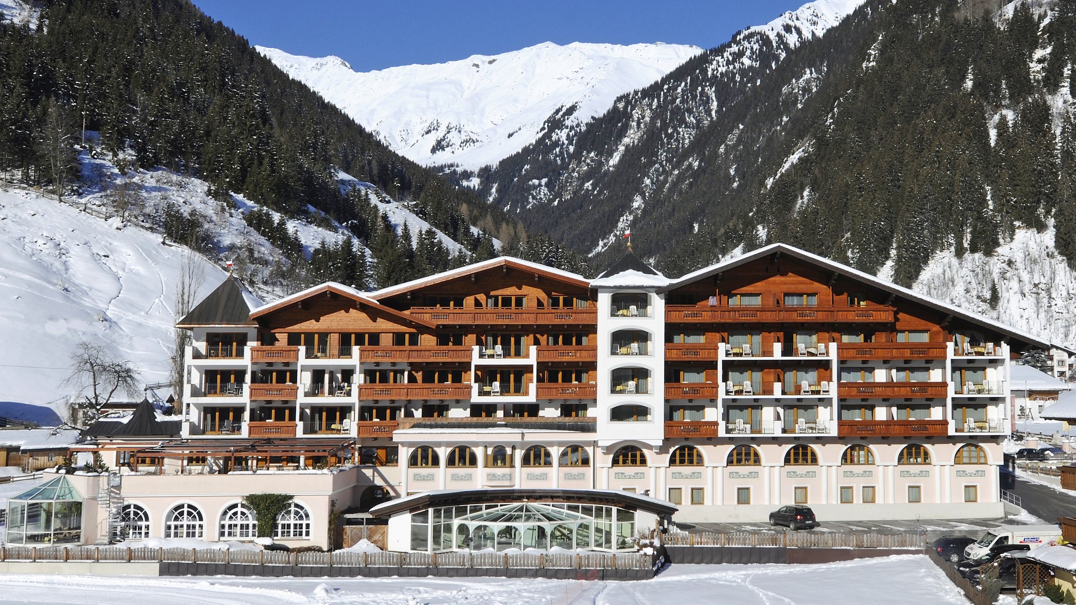 Stubaital: das Hotel mit Pool Großes Hotel in verschneitem Tal mit bewaldeten Bergen und blauem Himmel