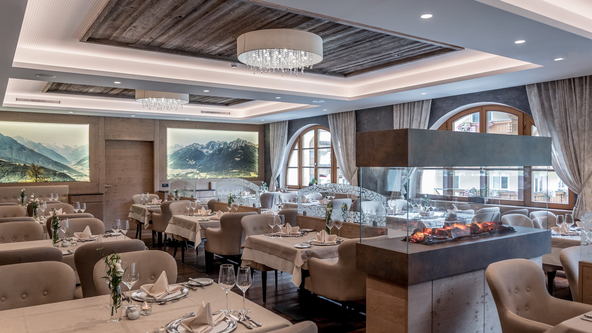 Stubaital: das Hotel mit Pool Elegantes Restaurant mit Kamin, gedeckten Tischen und Bergmotiven an der Wand
