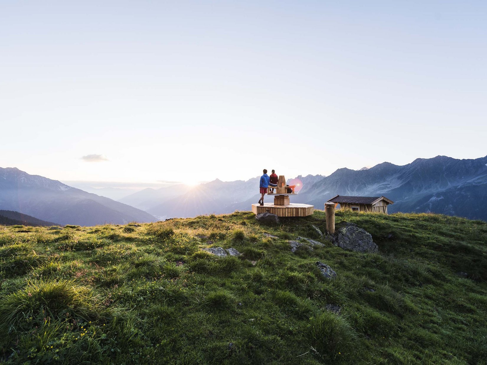 Stubaital: das Hotel mit Pool Zwei Menschen auf einem Holzpodest in den Bergen bei Sonnenuntergang