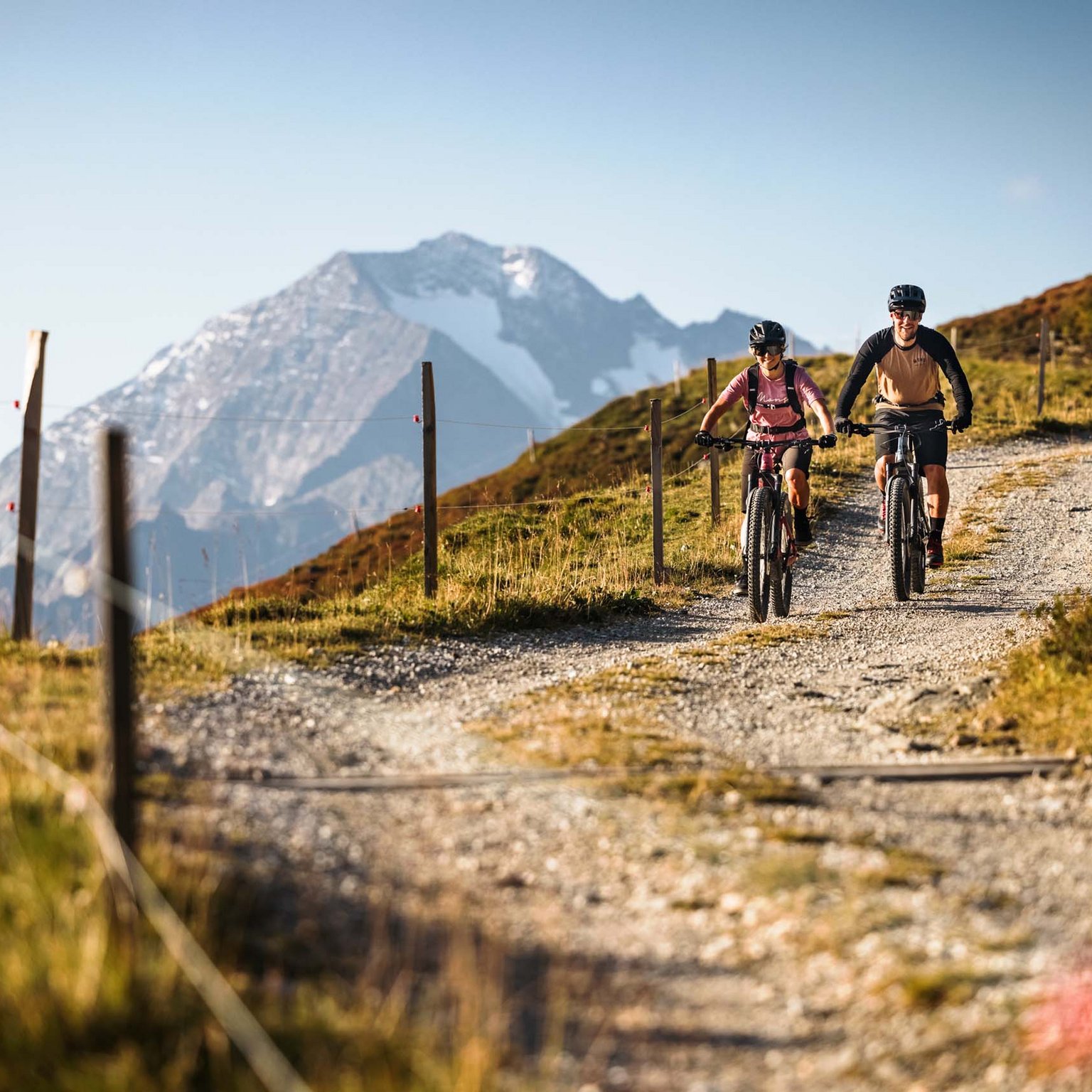 Stubaital: das Hotel mit Pool Zwei Mountainbiker fahren auf einem Bergweg mit schneebedecktem Gipfel im Hintergrund
