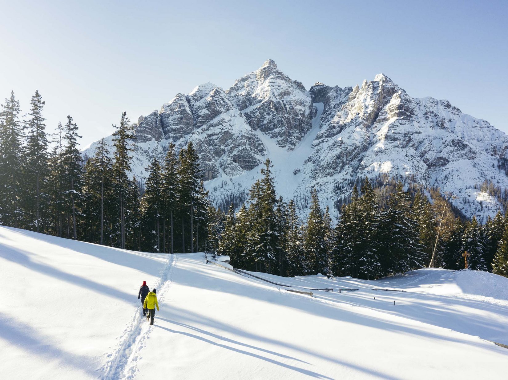 Stubaital: das Hotel mit Pool Zwei Personen wandern durch verschneite Landschaft vor bewaldeten Bergen