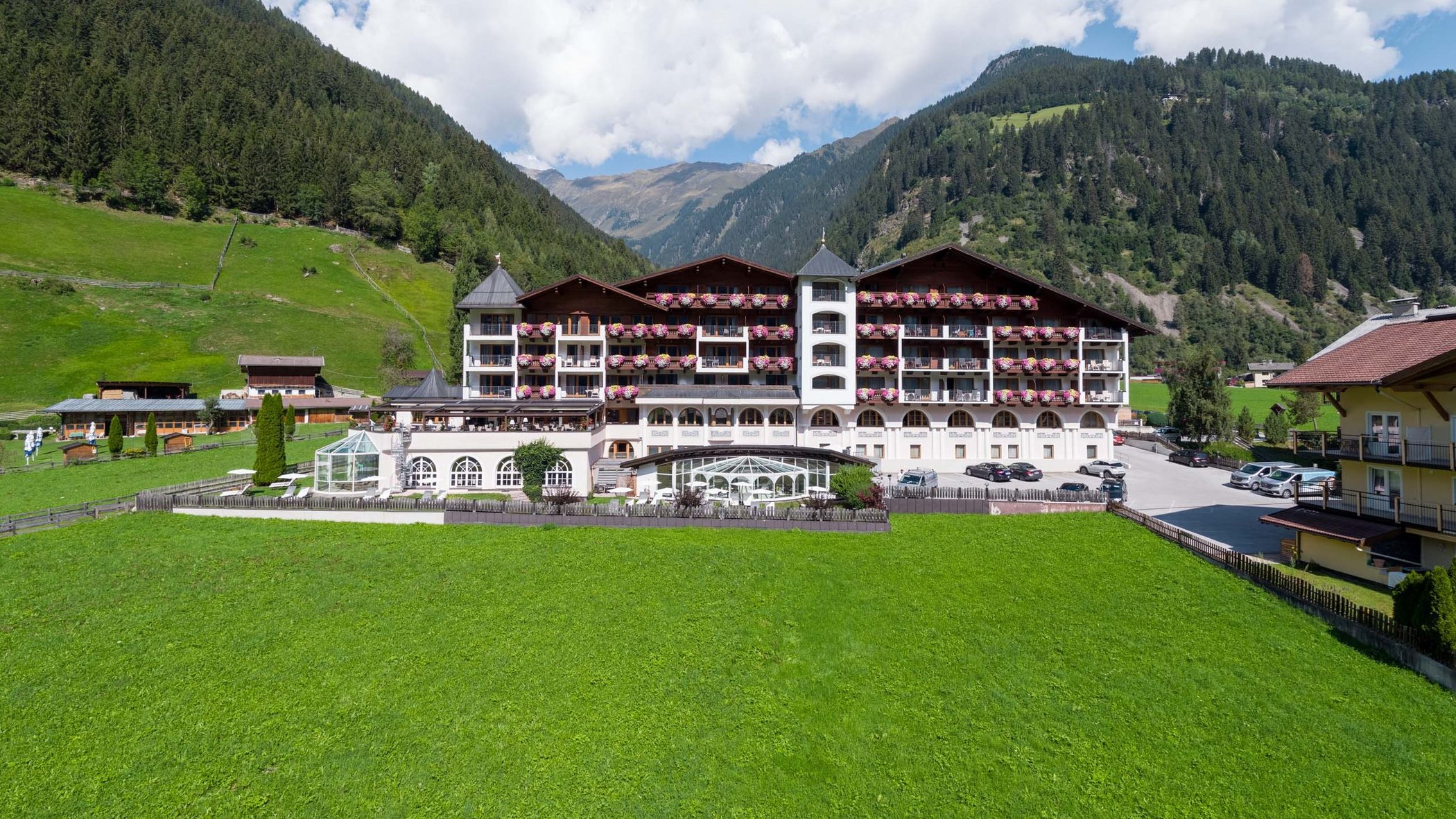 Stubaital: das Hotel mit Pool Hotel in grüner Berglandschaft mit blauem Himmel und weißen Wolken
